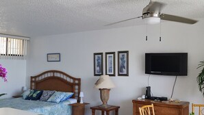 Un dormitorio con cama, mesita de noche, lámpara, televisor y un escritorio con silla.
