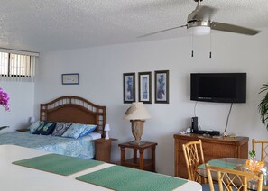A bedroom with a bed, bedside table, lamp, TV, and a desk with a chair.