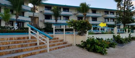 Un hôtel doté d’une piscine, d’un escalier menant à l’entrée et offrant une vue sur la plage.