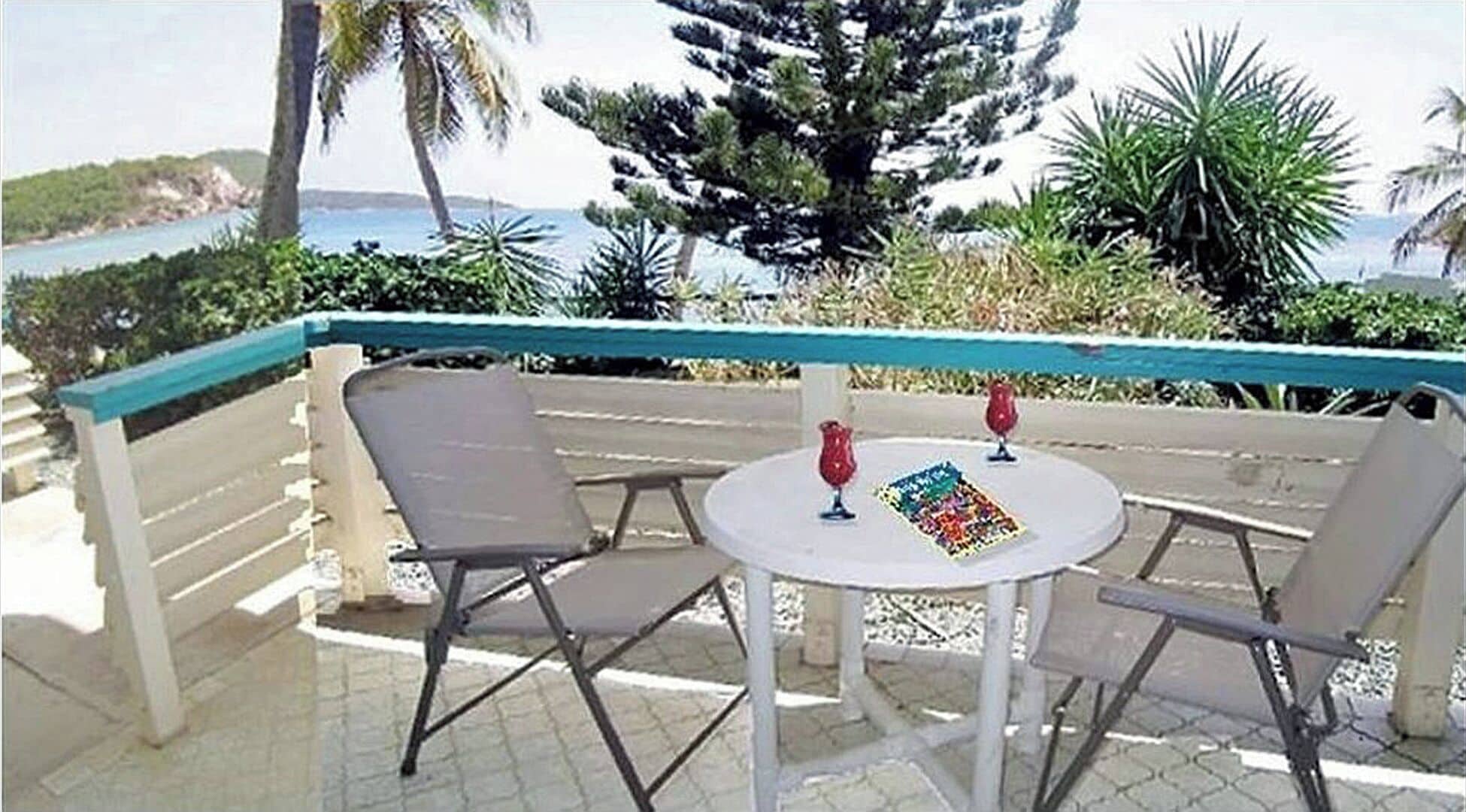 A balcony with two chairs and a table, a view of the sea, and a palm tree.