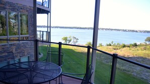A balcony with a table and chairs, overlooking a body of water and a grassy area.