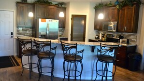 A modern kitchen with a central island, bar stools, stainless steel appliances, and wooden cabinets.