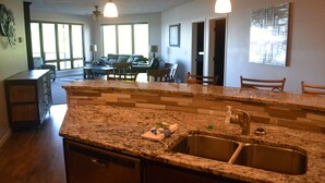 A kitchen with granite countertops, a stainless steel sink, and a dining area with a table and chairs.