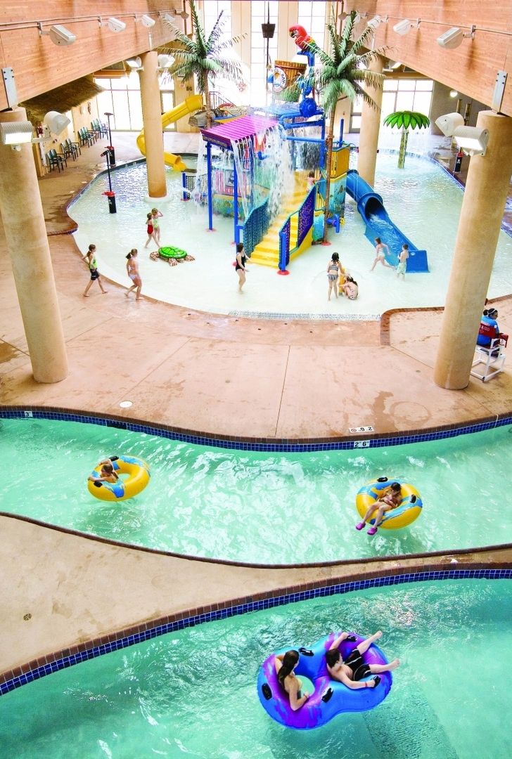 Parque acuático interior con varias piscinas, toboganes y zonas de juegos de agua.