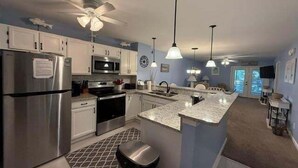 A modern kitchen with stainless steel appliances, a central island, pendant lighting, and a ceiling fan.