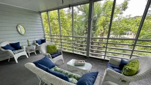 A spacious balcony with wicker furniture and large windows offering a view of greenery.