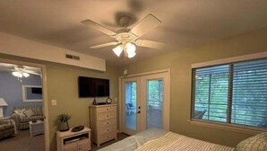 A bedroom with a bed, a ceiling fan, a dresser, a television, and a window with blinds.