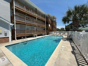 A rectangular swimming pool adjacent to a multi-story building with balconies. - Colony Iii 203 2 Bedroom Condo by RedAwning (Surfside Beach)
