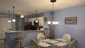 A dining area with a round table, four chairs, a kitchen in the background, and pendant lighting.
