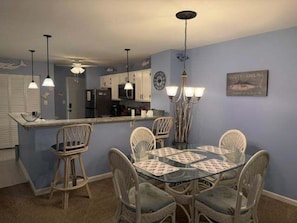 A dining area with a round table, four chairs, a kitchen in the background, and pendant lighting.