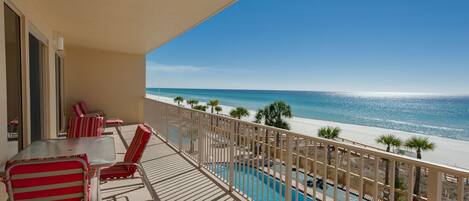 A balcony with a pool, red striped chairs, and a view of the beach and ocean.