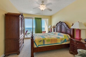 A bedroom with a wooden bed, a ceiling fan, a nightstand, and a view of the ocean through a sliding door.