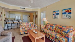 A living room with a sofa, a coffee table, and a dining area with chairs and a kitchen in the background. - Oceanfront Condo with Spacious Balcony - Unit 0306 by RedAwning (Panama City Beach)