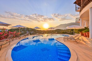A swimming pool with lounge chairs and umbrellas, surrounded by potted plants and a view of the sunset. - Hill House Adult Only (Kas)