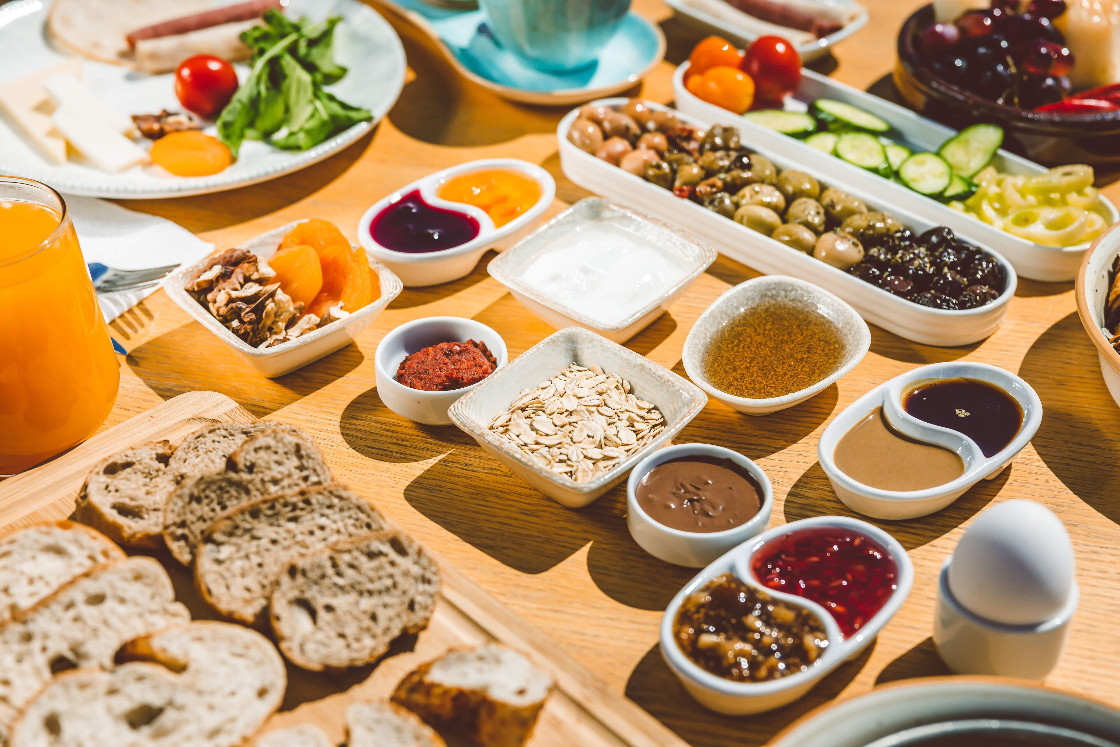 A table with various food items and condiments, including bread, olives, and sliced vegetables.