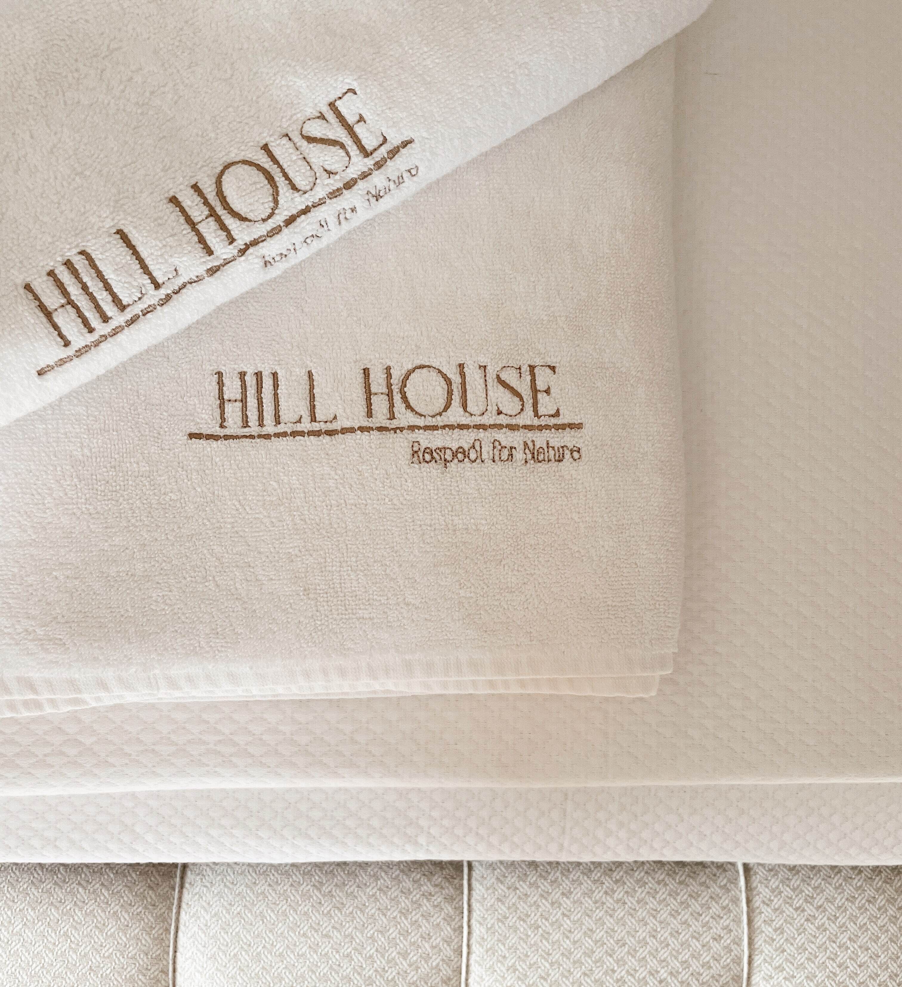 Stof met borduurwerk met de tekst 'HILL HOUSE' en 'Gerespecteerd voor de Natuur'.