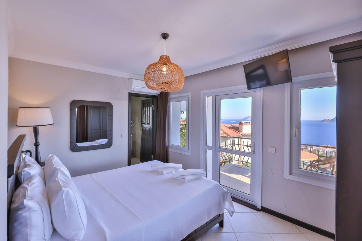 A bedroom with a bed, a hanging light fixture, a TV mounted on the wall, and a balcony with a view.