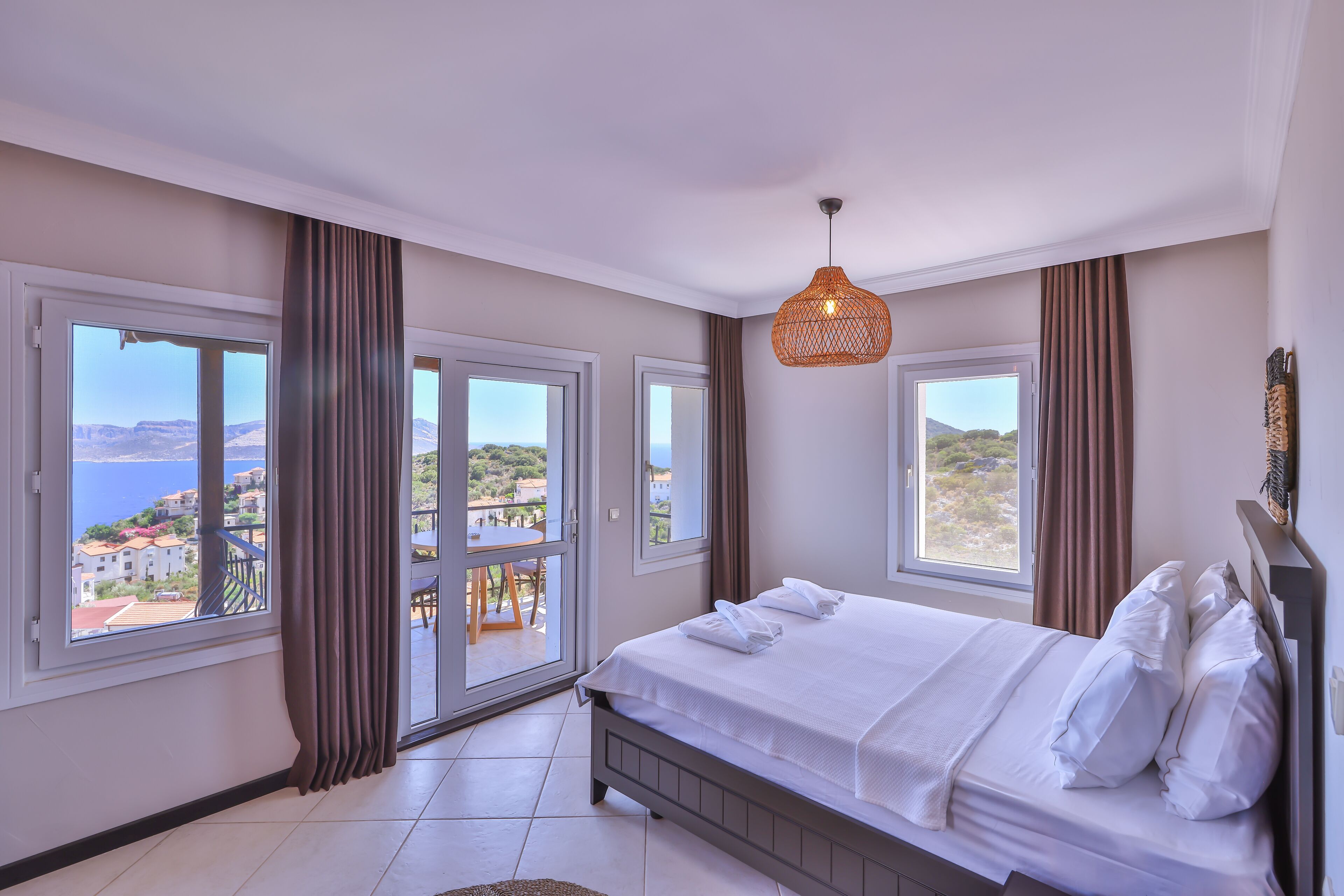 A bedroom with a bed, large windows, and a view of the sea.