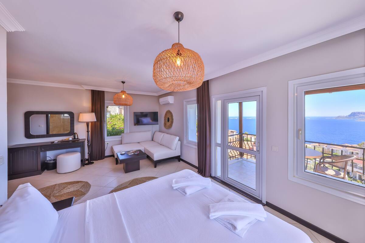 A hotel room with a bed, a sofa, a desk, and a large window with a view of the sea.