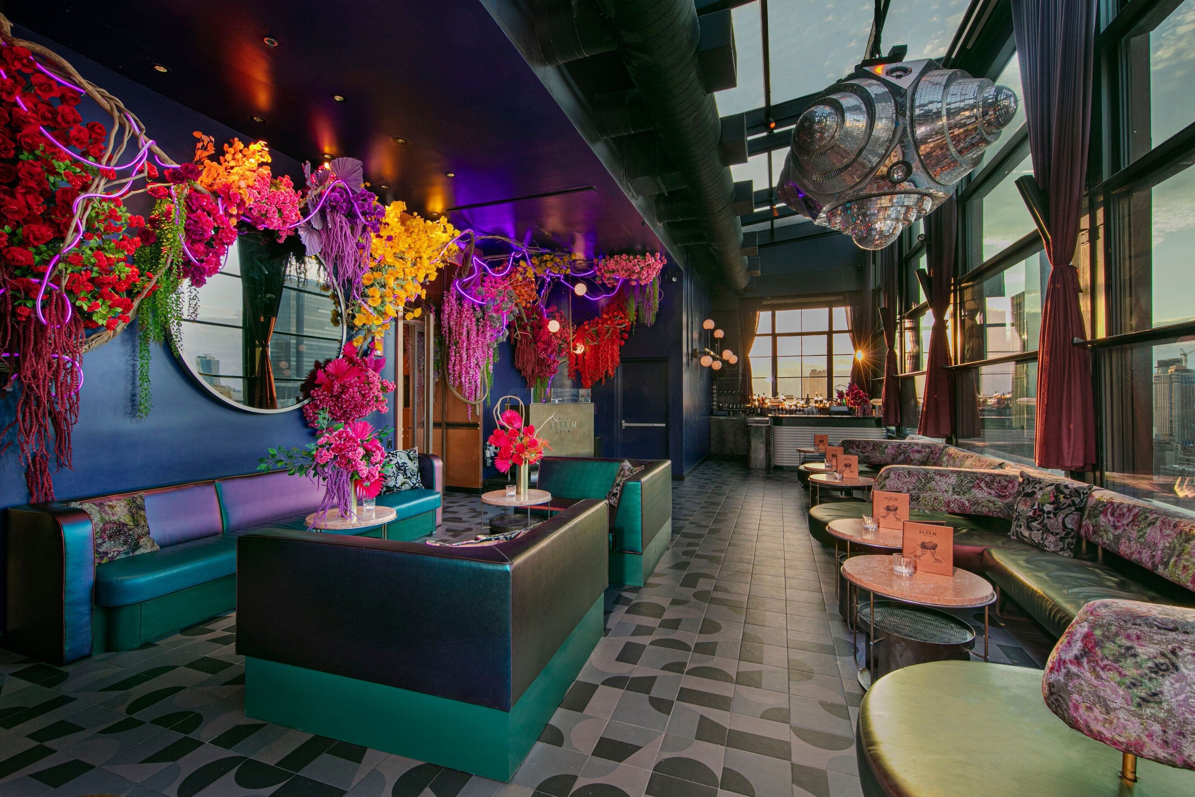 A modern lounge area with teal sofas, a central bar, and vibrant floral arrangements.