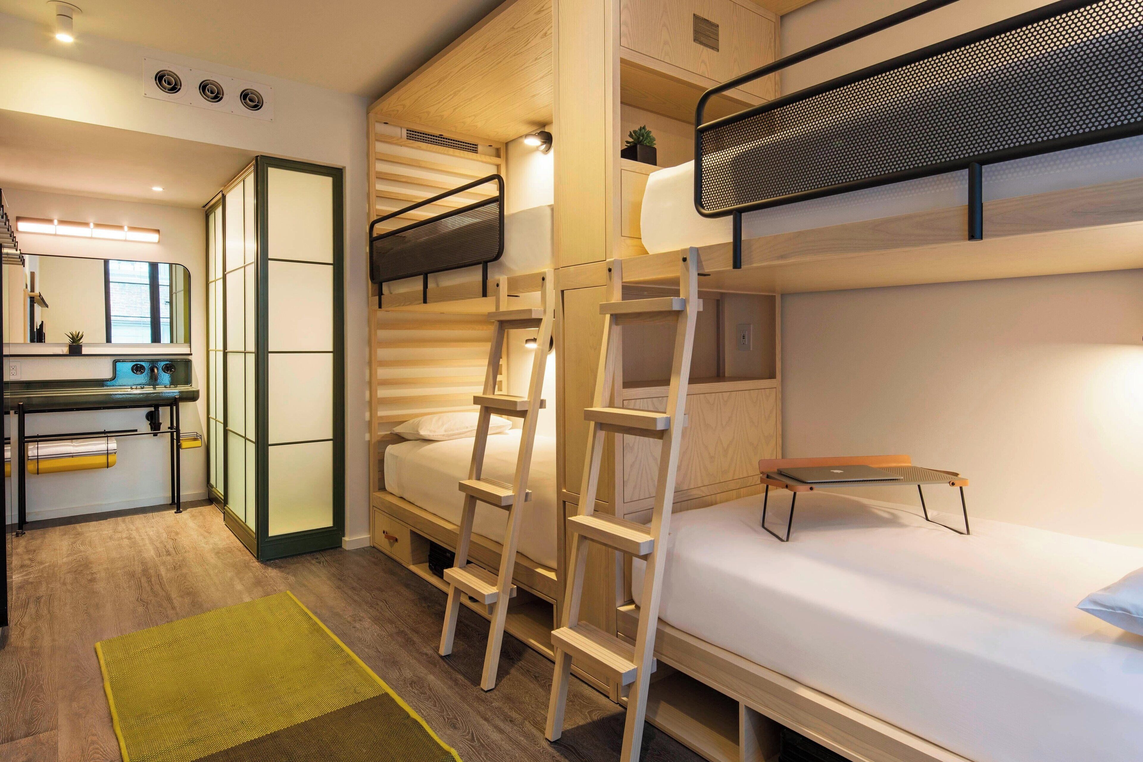 A compact hotel room with bunk beds, a small desk, and a mirror.