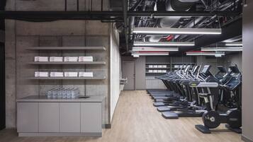 A gym with treadmills, a water station, and a concrete wall with shelves.