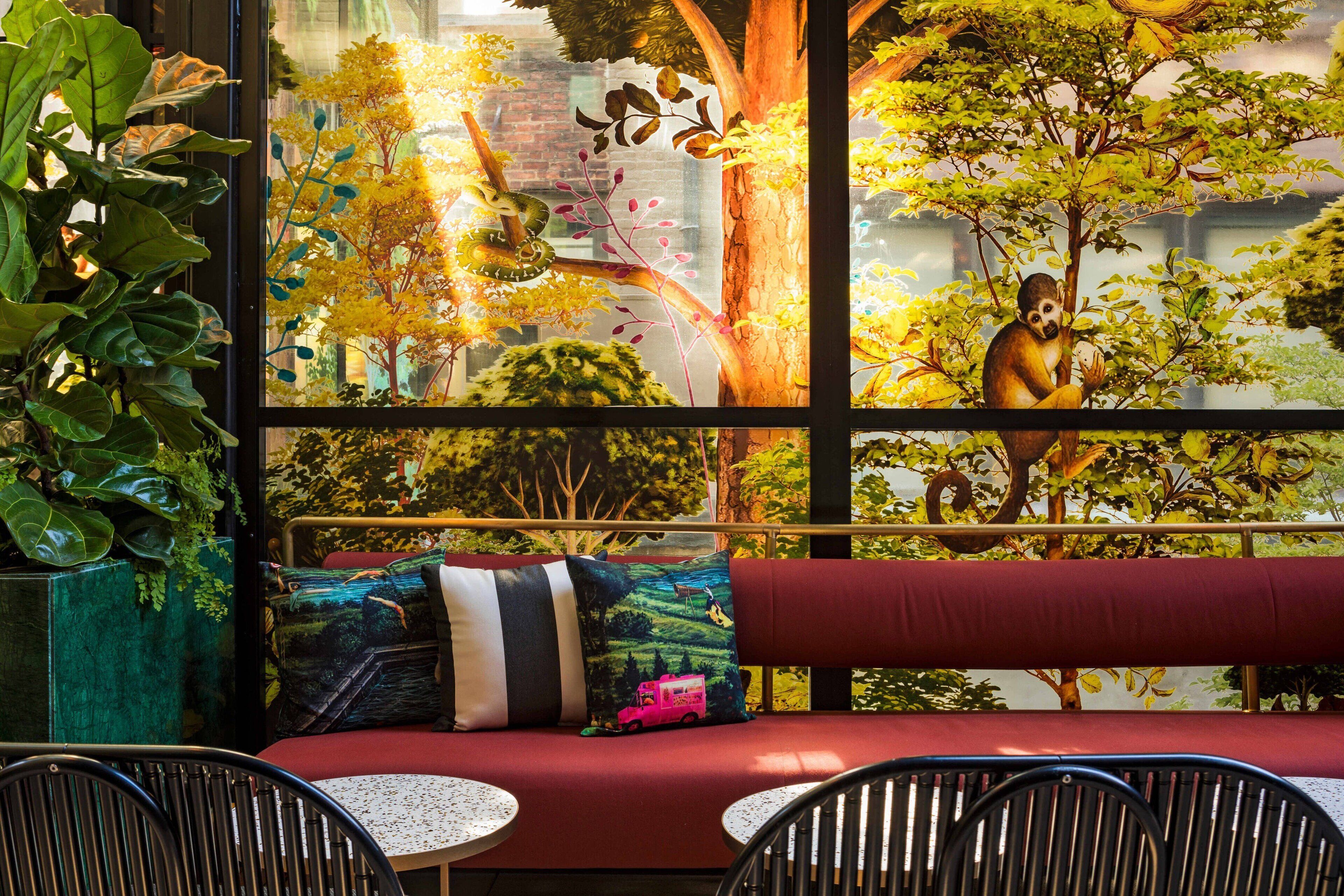 A seating area with a red bench, two round tables, and a large window with a mural of a monkey and trees.