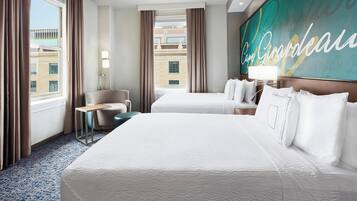 A hotel room with two beds, a desk, a chair, and a large window with curtains.