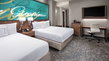 A hotel room with two beds, a desk, a chair, a TV, and a bathroom visible in the background.