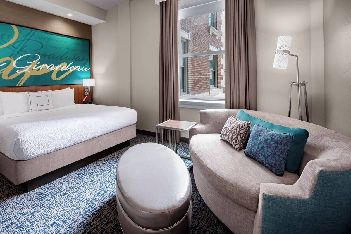 Ein Hotelzimmer mit Bett, Sofa, kleinem Tisch und einem Fenster mit Vorhängen.