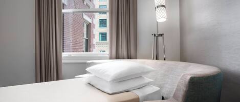 A hotel room with a single bed, a chair, a bedside lamp, and a window with curtains.