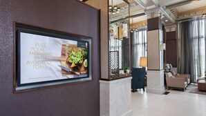 Un hall d’hôtel moderne avec une affiche encadrée faisant la publicité du petit-déjeuner au nouveau Bistro, un coin salon avec des canapés et une table basse, et un miroir décoratif qui reflète l’espace.