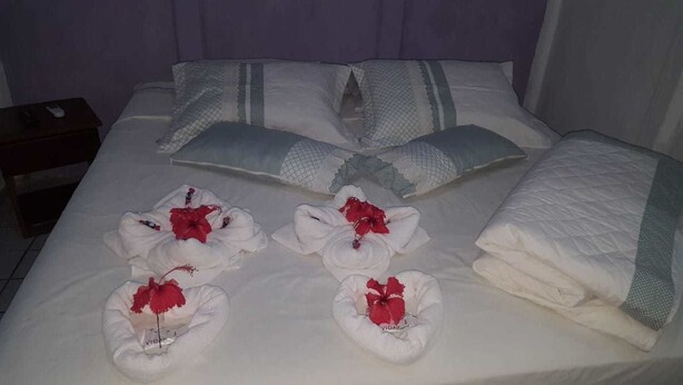 A neatly made bed with white linens, pillows, and a blanket. There are towels with red flowers placed on the bed. - Pousada Água Viva (Fernando de Noronha)