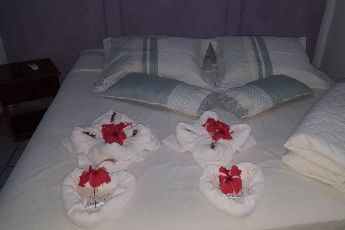 Ein ordentlich bezogenes Bett mit weißen Leinen, Kissen und einer Decke. Auf dem Bett liegen Handtücher mit roten Blumen.