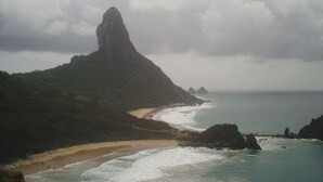 A coastal landscape with a prominent rock formation, a sandy beach, and the ocean. - Pousada Água Viva (Fernando de Noronha)