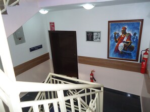 A staircase with a white railing, a fire extinguisher mounted on the wall, a framed painting, and a sign indicating the location of the professor's office. - Saheeto Suites (Lagos)