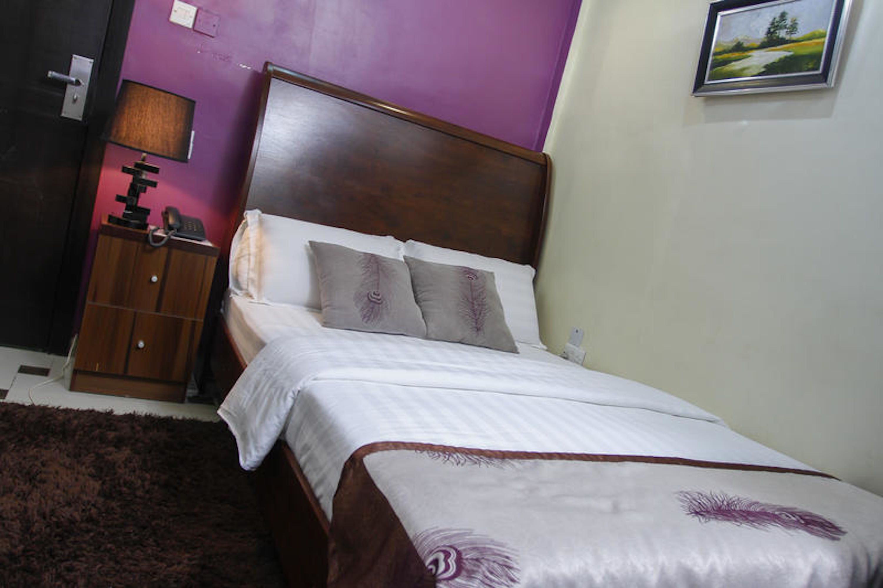 A neatly made bed with a wooden headboard, a small bedside table with a lamp, and a framed picture on the wall.
