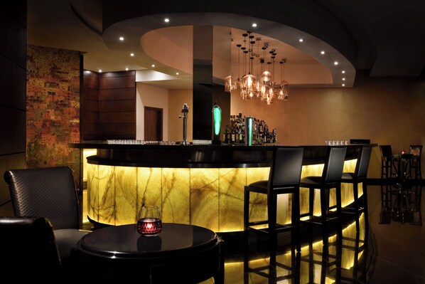 A bar area with a marble countertop, multiple bar stools, and a hanging light fixture. - Accra Marriott Hotel (Accra)