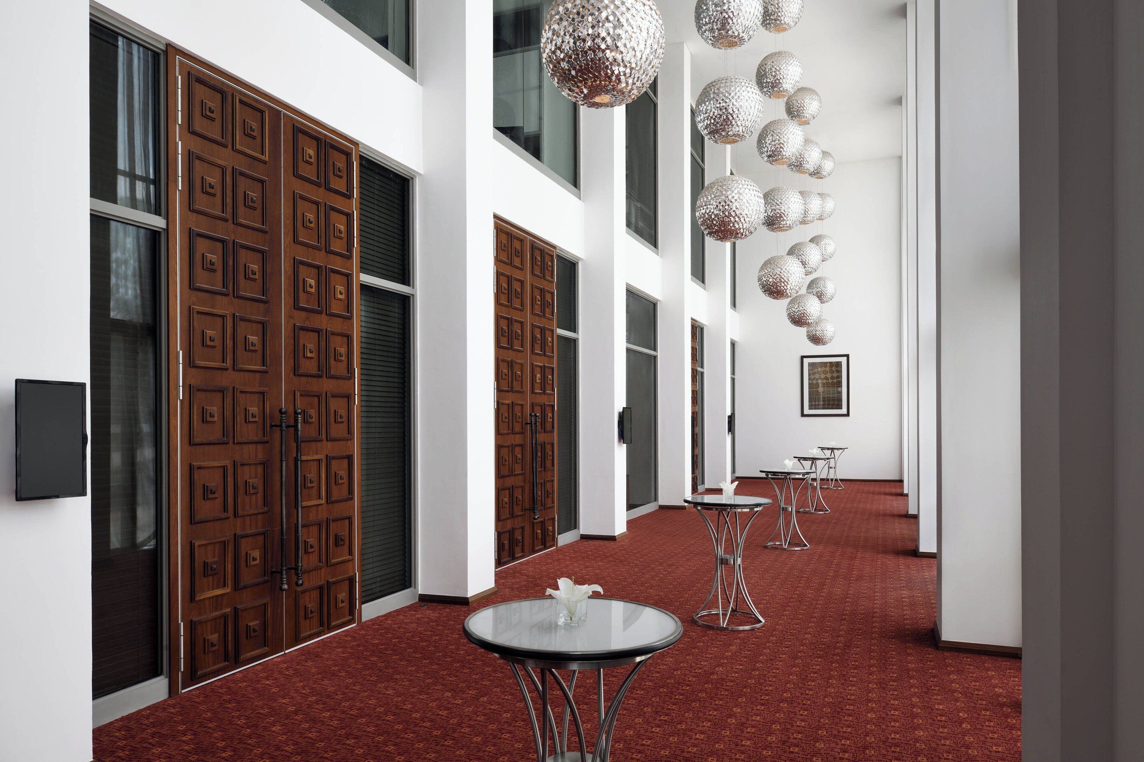 A hallway with a red carpet, wooden doors, and modern pendant lights.
