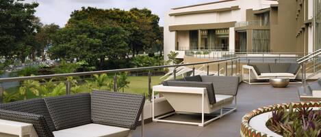A rooftop terrace with outdoor seating, a view of the surrounding greenery, and a modern building in the background.
