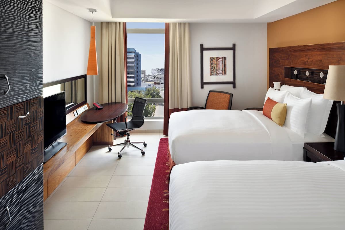 Une chambre d’hôtel avec deux lits, un bureau avec une télévision, une chaise et une vue sur la ville.