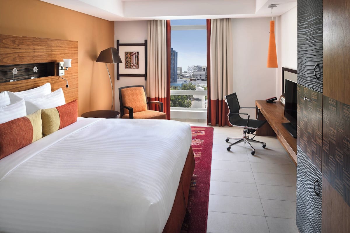 Une chambre d’hôtel avec un grand lit, un bureau avec une chaise, une télévision et une vue sur la ville par la fenêtre.