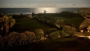 A nighttime view of a coastal area with a prominent lighthouse, a well-maintained grassy area, and a clear view of the ocean. - Stunning pool and ocean views await you in this beautiful, convenient condo. (Wrightsville Beach)