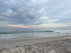 A beach with waves, a cloudy sky, and a sunset. - Stunning pool and ocean views await you in this beautiful, convenient condo. (Wrightsville Beach)