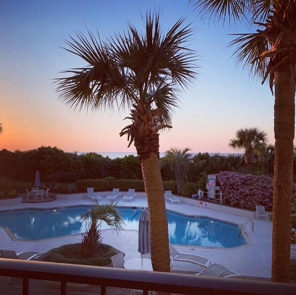 A pool area with lounge chairs and palm trees. - Stunning pool and ocean views await you in this beautiful, convenient condo. (Wrightsville Beach)