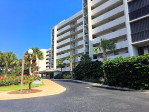 A multi-story hotel with a central courtyard, palm trees, and a clear blue sky. - Stunning pool and ocean views await you in this beautiful, convenient condo. (Wrightsville Beach)