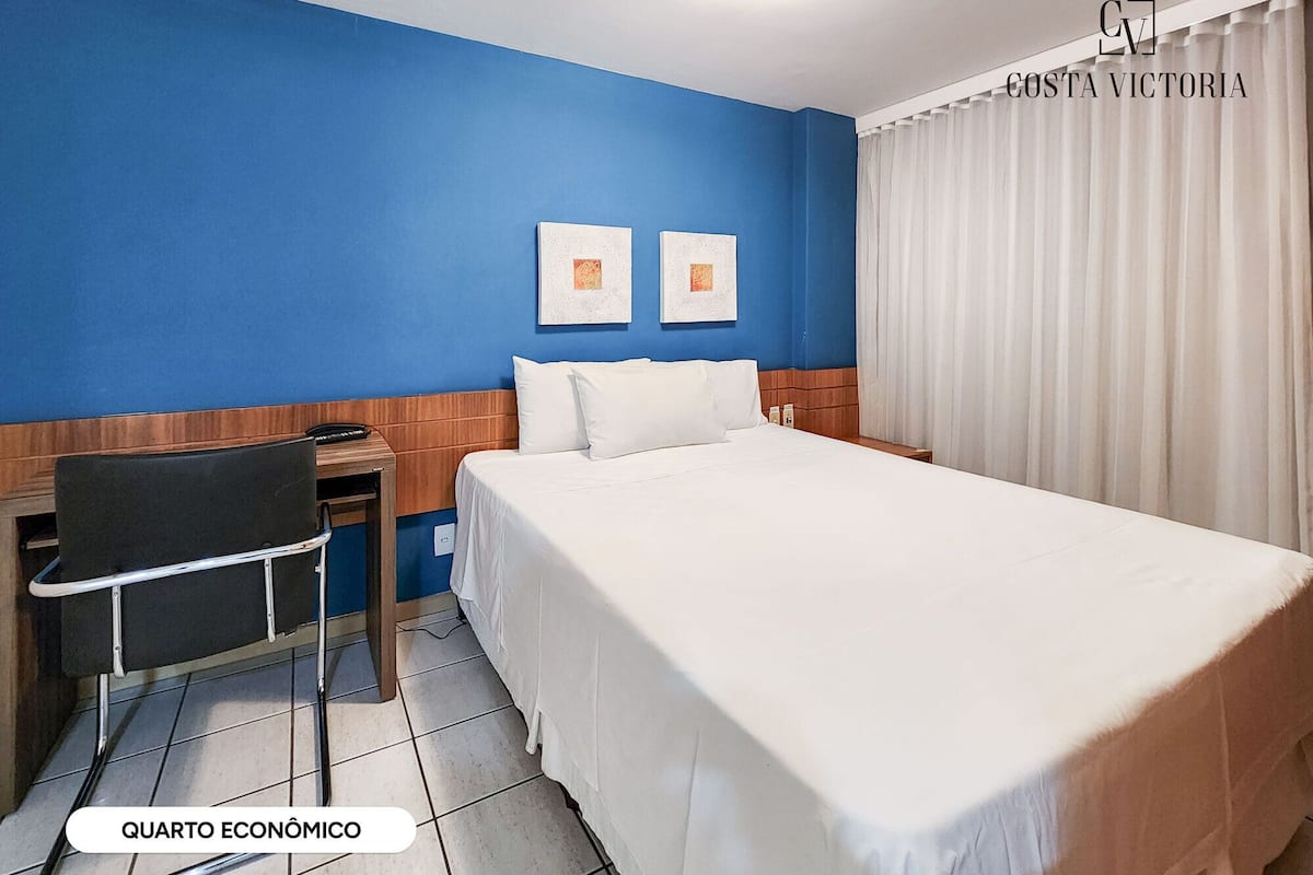 A hotel room with a large bed, a desk, and two framed pictures on the wall.