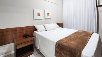 Hotellihuone, jossa on sänky, puinen yöpöytä, puhelin ja ruskea huopa.
