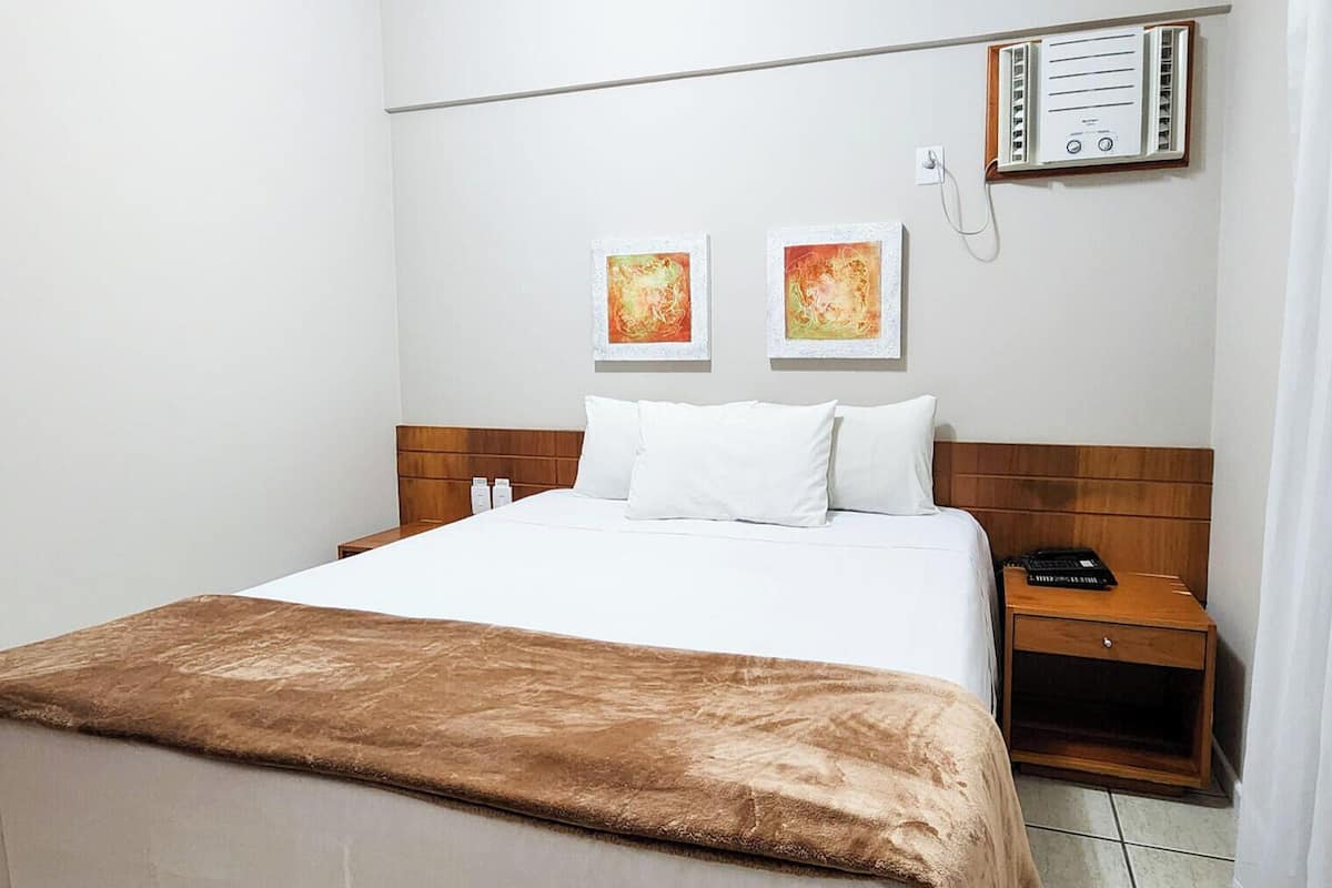 A hotel room with a bed, bedside tables, a thermostat, and artwork on the wall.