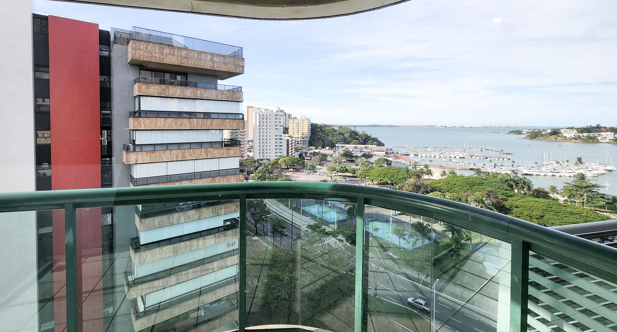 Vista de uma varanda sobre uma marina e edifícios, com uma placa indicando "QUARTO CASAL AMPLO".